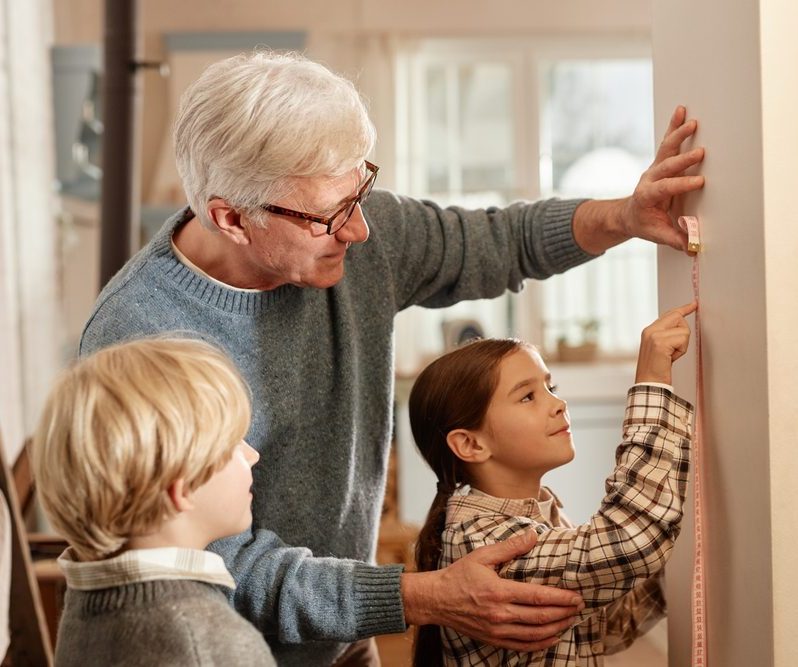 Young woman in cozy sweater decorating potted Christmas tree with small glass baubles in light modern Scandinavian interior. Eco-friendly winter holidays. Christmas tree in a pot. Selective focus